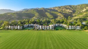 A large, well-maintained golf course with a series of white buildings with multiple stories and balconies, surrounded by lush greenery and mountains in the background. - The Polo Lounge By The Sea 3BD w Large Patio (Carpinteria)
