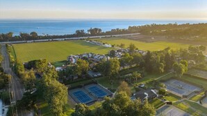 An aerial view of a residential area with houses, tennis courts, and a large green field. - The Polo Lounge By The Sea 3BD w Large Patio (Carpinteria)