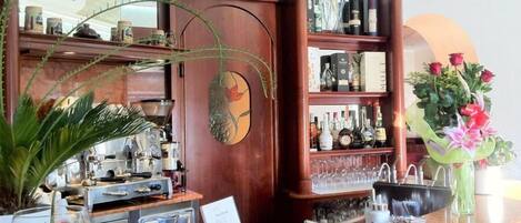Zona de bar con estantes llenos de botellas de licor, una caja registradora y una planta en maceta.