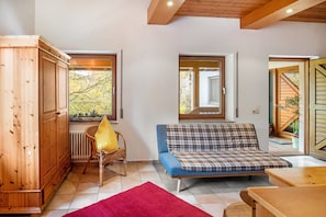 Una habitación con un armario de madera, una silla de mimbre con cojín amarillo, un sofá azul y un tapete rojo.