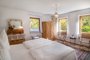 Une chambre avec un grand lit, une armoire en bois, un bureau avec une chaise et une fenêtre donnant sur un paysage verdoyant.