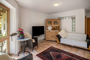 A living room with a TV, sofa, wooden cabinet, and a dining table with a flower vase.