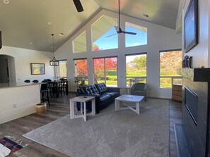A spacious living room with a high ceiling, large windows, a ceiling fan, a black leather sofa, a white coffee table, and a dining area with a table and chairs. - Great location, golf or Temple and newly remodeled. 3 bed, 3 bath in Snowflake (Snowflake)