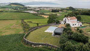 Une maison moderne avec une piscine, entourée de champs verdoyants et offrant une vue sur la mer.