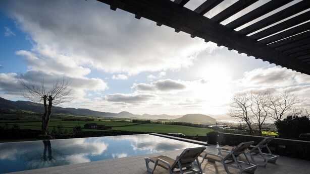 Une piscine à débordement avec des chaises longues, offrant une vue sur un paysage verdoyant et des montagnes.