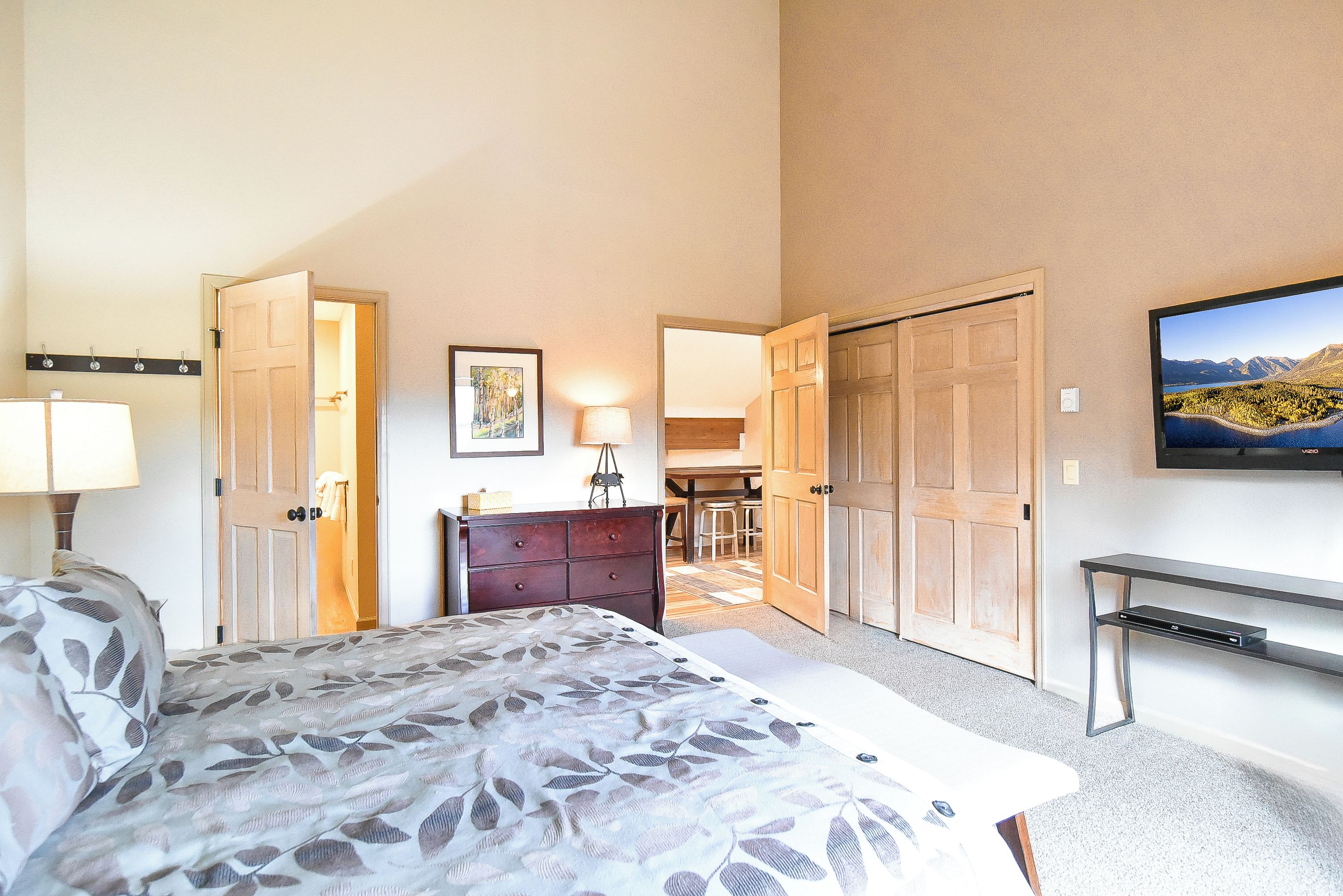 A hotel room with a bed, a desk, a chair, a TV, and a door leading to a balcony.