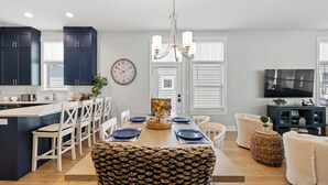 A modern kitchen with dark cabinets, a wooden dining table set with blue plates, and a chandelier. - Harbor Shores 3BR in St. Joseph | Community Pool, Sleeps 8, Near Silver Beach (St Joseph)