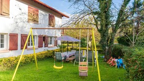 A house with a swing set, a table with chairs, and a garden.