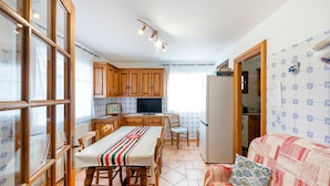 A compact kitchen with wooden cabinets, a dining table, and a sofa with a patterned cushion.
