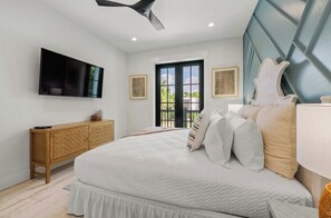 A bedroom with a bed, a wooden cabinet, a flat-screen TV, and a ceiling fan. - New 8/8 bathroom beach house! Heated pool and spa! (Sarasota)