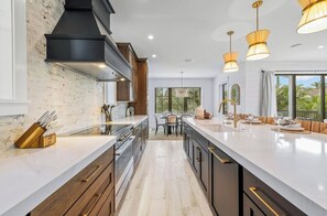 Una cocina moderna con una isla grande, armarios de madera e iluminación colgante.