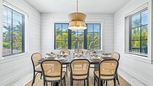A dining room with a large table set for six, surrounded by wicker chairs, with a pendant light above.
