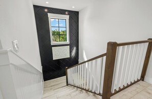 Una escalera con barandilla blanca y pared negra con un ventanal.