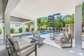 A modern outdoor pool area with a spiral staircase, lounge chairs, and a clear view of the surrounding greenery. - New 8/8 bathroom beach house! Heated pool and spa! (Sarasota)