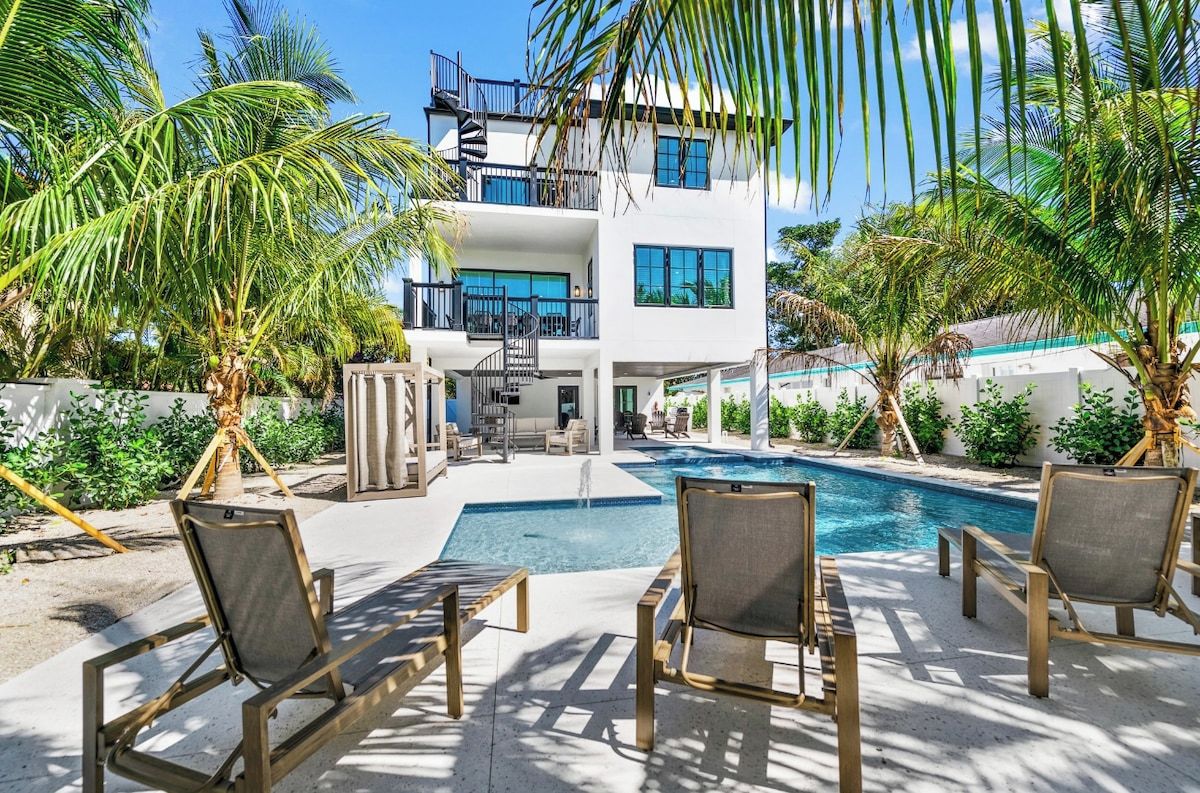 A modern building with a pool, outdoor seating, and palm trees.