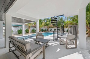 A modern outdoor pool area with a spiral staircase, lounge chairs, and a clear view of the pool. - New 8/8 bathroom beach house! Heated pool and spa! (Sarasota)