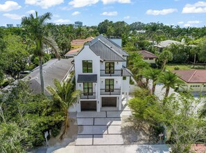 A multi-story residential building with a balcony, surrounded by lush greenery and palm trees. - New 8/8 bathroom beach house! Heated pool and spa! (Sarasota)