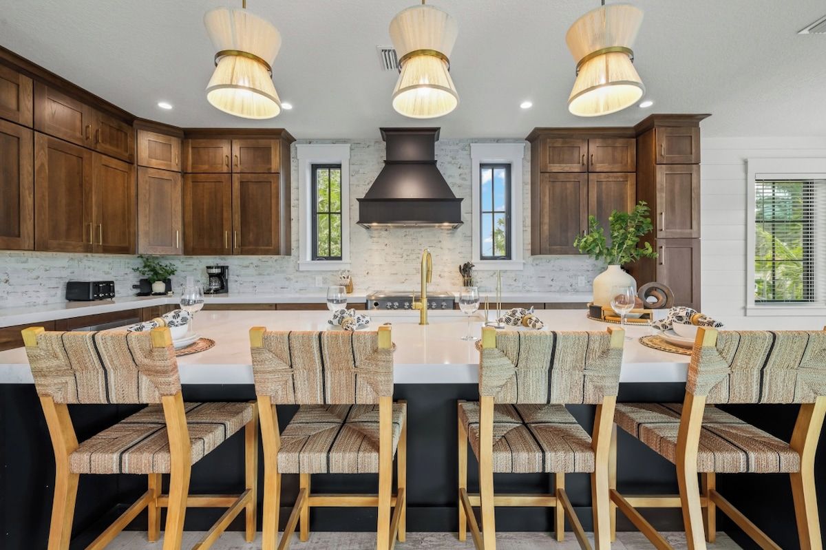 Una cocina con armarios de madera, una isla central con sillas, iluminación colgante y una campana extractora negra.