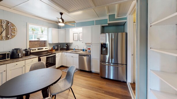 A modern kitchen with white cabinets, stainless steel appliances, a wooden clock, and a dining area with a table and chairs. - 4297 Earney Rd, Unit 3, Woodstock (Woodstock)
