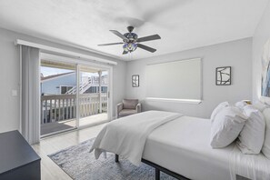 Une chambre à coucher avec un lit, un ventilateur de plafond, une chaise, une fenêtre et une vue sur un balcon.