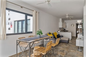 A modern kitchen with a dining area, a sofa, and a ceiling fan.