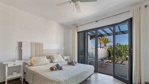 A bedroom with a bed, bedside tables, a ceiling fan, and a sliding glass door leading to an outdoor patio. - Casa Bidasoa 35: Sea Views, Shared Pool & Wi-Fi in Playa Blanca (Playa Blanca)