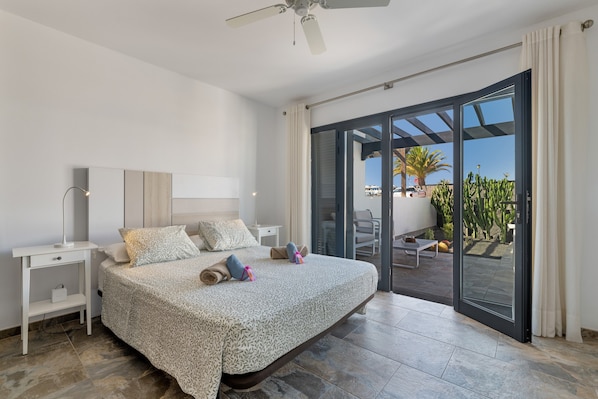 A bedroom with a bed, bedside tables, a ceiling fan, and a sliding glass door leading to an outdoor patio.