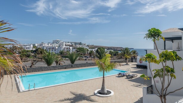 A pool area with a view of the sea and buildings in the background. - Casa Bidasoa 35: Sea Views, Shared Pool & Wi-Fi in Playa Blanca (Playa Blanca)