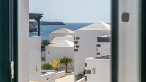 A coastal view with white buildings, a palm tree, and a rocky cliff. - Casa Bidasoa 35: Sea Views, Shared Pool & Wi-Fi in Playa Blanca (Playa Blanca)