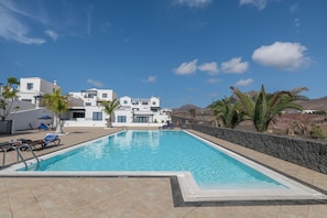 A swimming pool with lounge chairs, a stone wall, and a building with a white facade.