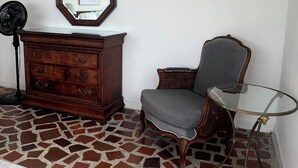 A room with a wooden dresser, a chair, a glass table, and a floor with a mosaic pattern.