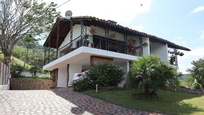 A two-story house with a balcony, a stone wall, and a paved driveway.