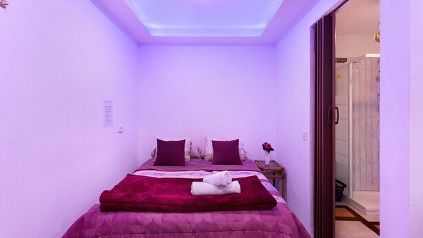 A bedroom with a bed, pillows, a blanket, a nightstand, and a door leading to another room. - Studio 'Luci's House B' with Mountain Views, Shared Terrace, and Wi-Fi (São Jorge santana)