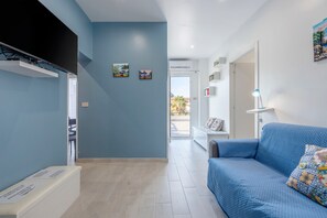 Un salon moderne avec un canapé bleu, un téléviseur à écran plat fixé au mur et une petite table avec une lampe.