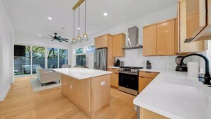 A modern kitchen with wooden cabinets, a central island, and a large window overlooking a deck. - Sleeps 20, 5br Pool table, Chef's Kitchen, Pool (Austin)