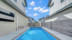 A rectangular swimming pool with a clear blue water surface, surrounded by light-colored walls with windows and a wooden fence in the background. - Sleeps 20, 5br Pool table, Chef's Kitchen, Pool (Austin)