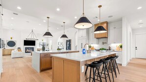 A modern kitchen with a central island, pendant lighting, and a seating area with bar stools. - 7BR Estate - Pool on Golf Course - 4mi to Downtown (Austin)