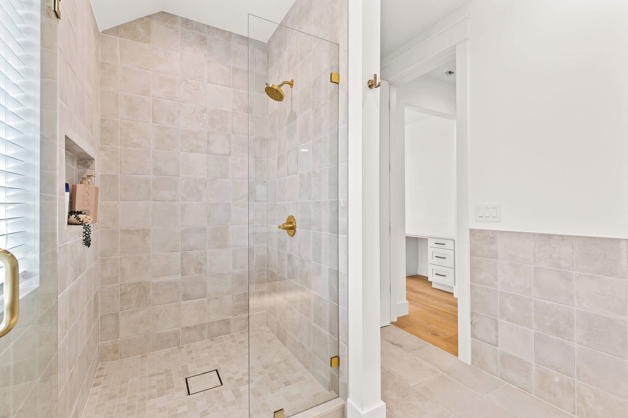A modern bathroom with a glass-enclosed shower, beige tiles, and a wooden floor.