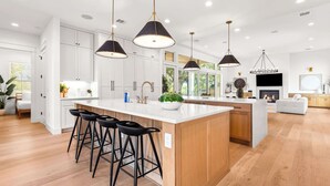A modern kitchen with a large island, black bar stools, pendant lighting, and a fireplace. - 7BR Estate - Pool on Golf Course - 4mi to Downtown (Austin)