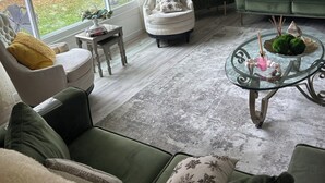A living room with a large window, a green sofa, a white armchair, and a glass coffee table with decorative items. - 2-bedroom townhome in charming South Milwaukee with AC (South Milwaukee)