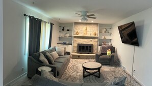 A living room with a grey sectional sofa, a round coffee table, a fireplace, and a mounted TV. - 2-bedroom townhome in charming South Milwaukee with AC (South Milwaukee)
