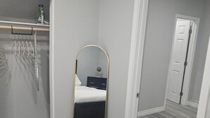 Ein Schlafzimmer mit einem Bett, einem Spiegel, einem Kleiderschrank und einer Tür zu einem anderen Raum.