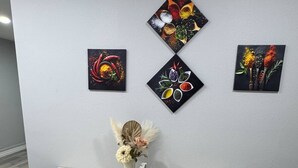 Ein Essbereich mit einem weißen Tisch und Bänken, einer Vase mit Blumen sowie drei an der Wand befestigten Gewürzbildern.