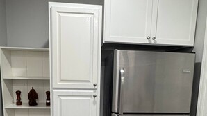 Eine Küche mit weißen Schränken, einem Edelstahlkühlschrank und einem Zweitürschrank.