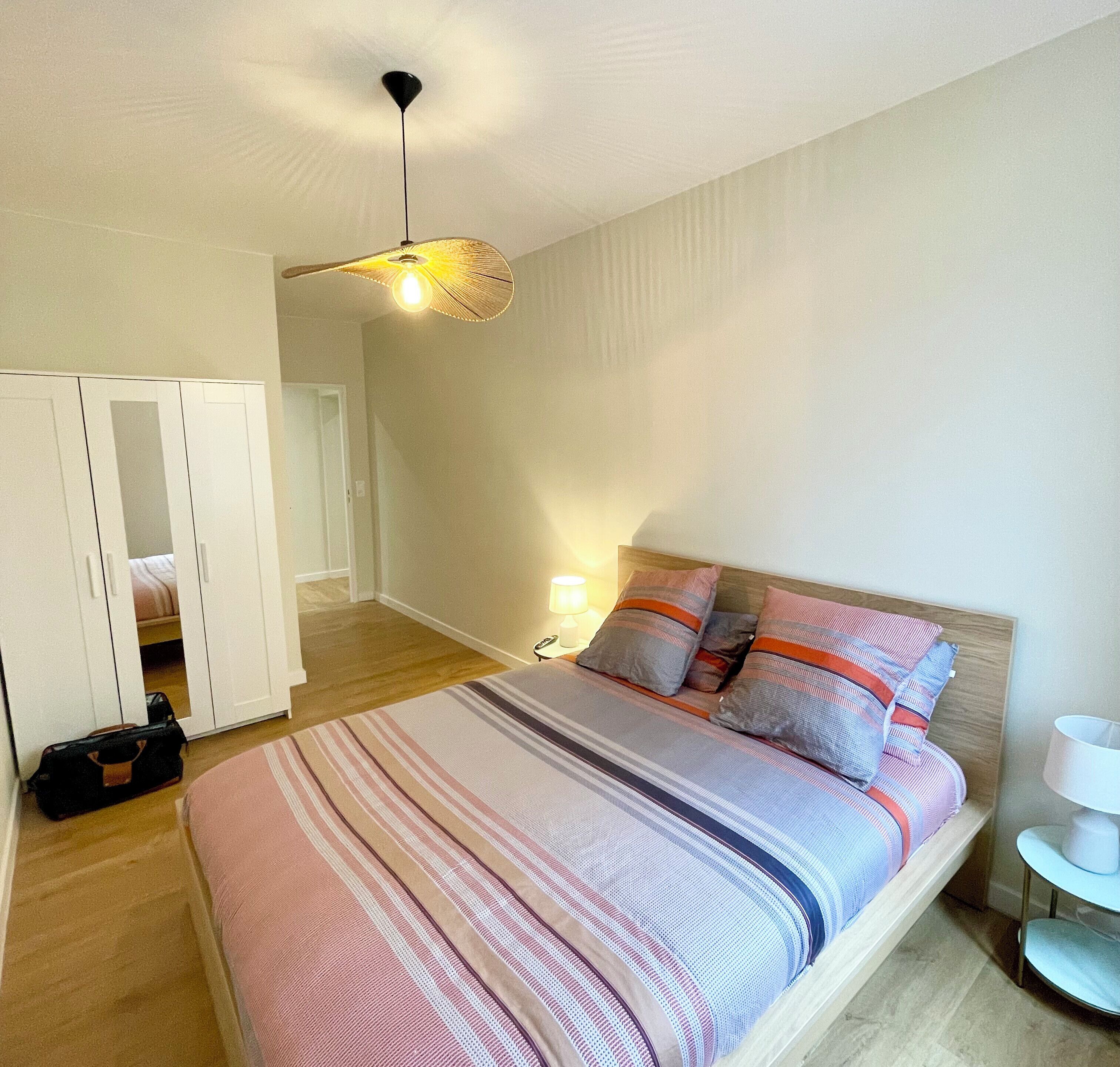 Une chambre à coucher comprenant un lit, une table de chevet, une lampe, une armoire et un ventilateur de plafond.