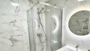 A modern bathroom with a glass-enclosed shower, a white sink, and a marble-tiled wall. - Casa Luna – 1 Bedroom, 4 Guests, City Center, Fully Equipped (Metz)