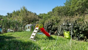 A playground with a slide, a small playhouse, and a swing set in a grassy area with trees in the background. - Villa 'Gite Les Bouches Rouges 6 Personnes' with Mountain View, Wi-Fi and Air Conditioning (Vesseaux)