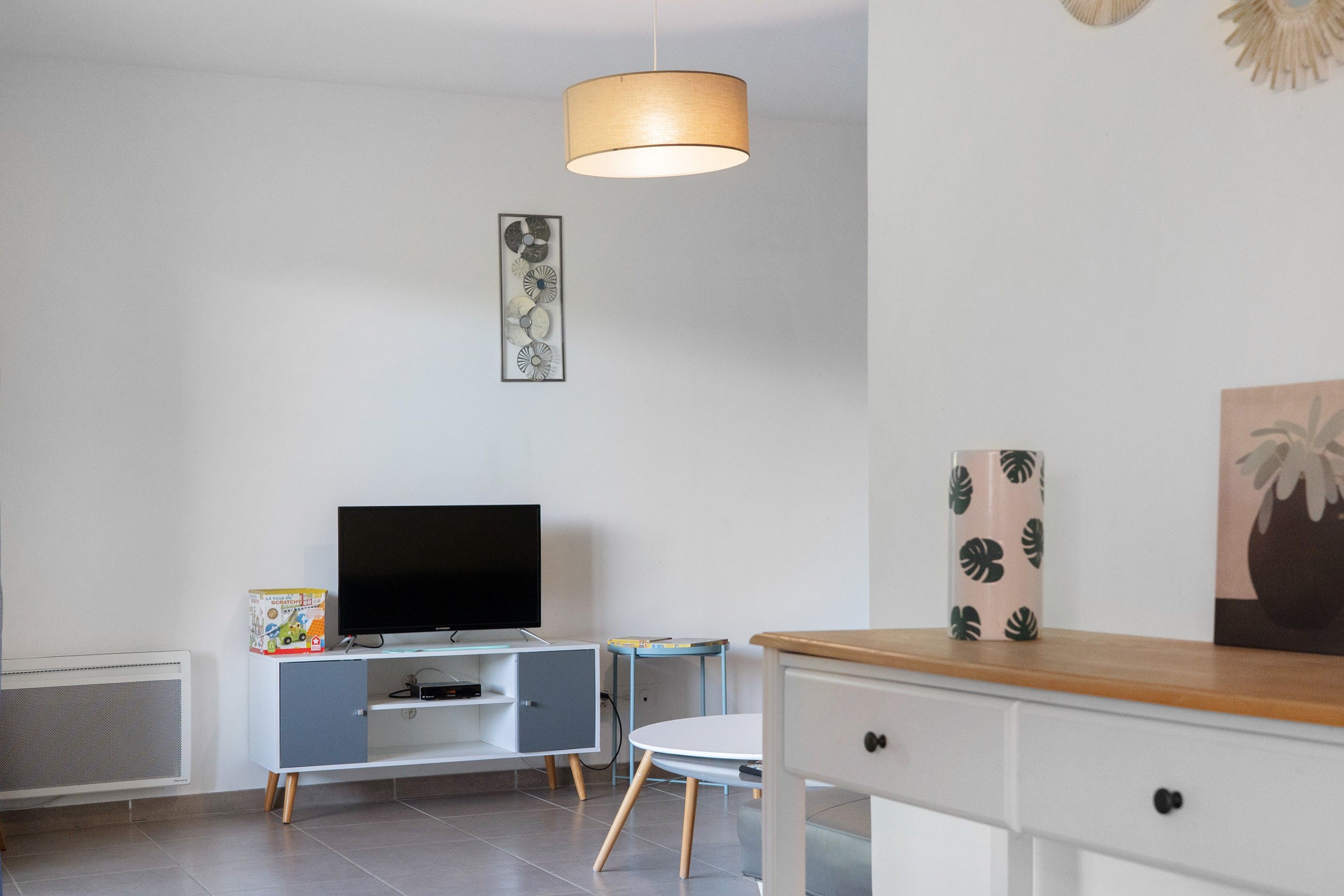 Un salon moderne avec un téléviseur à écran plat, un meuble, une table et une chaise.