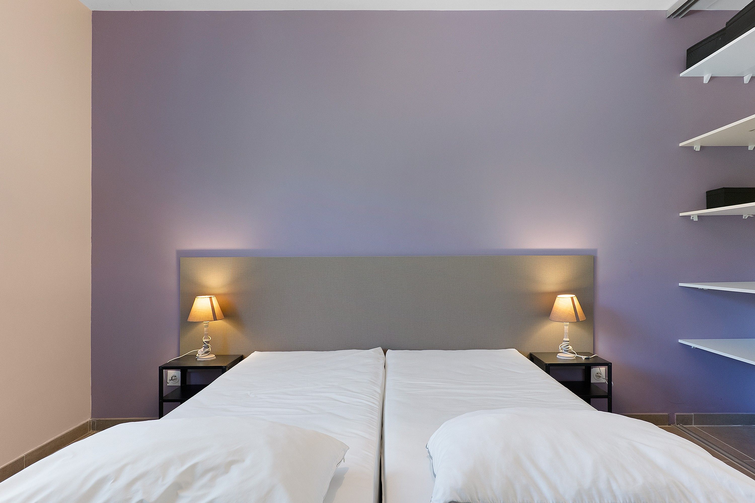 A hotel room with a double bed, two bedside tables with lamps, and built-in shelving on the wall.