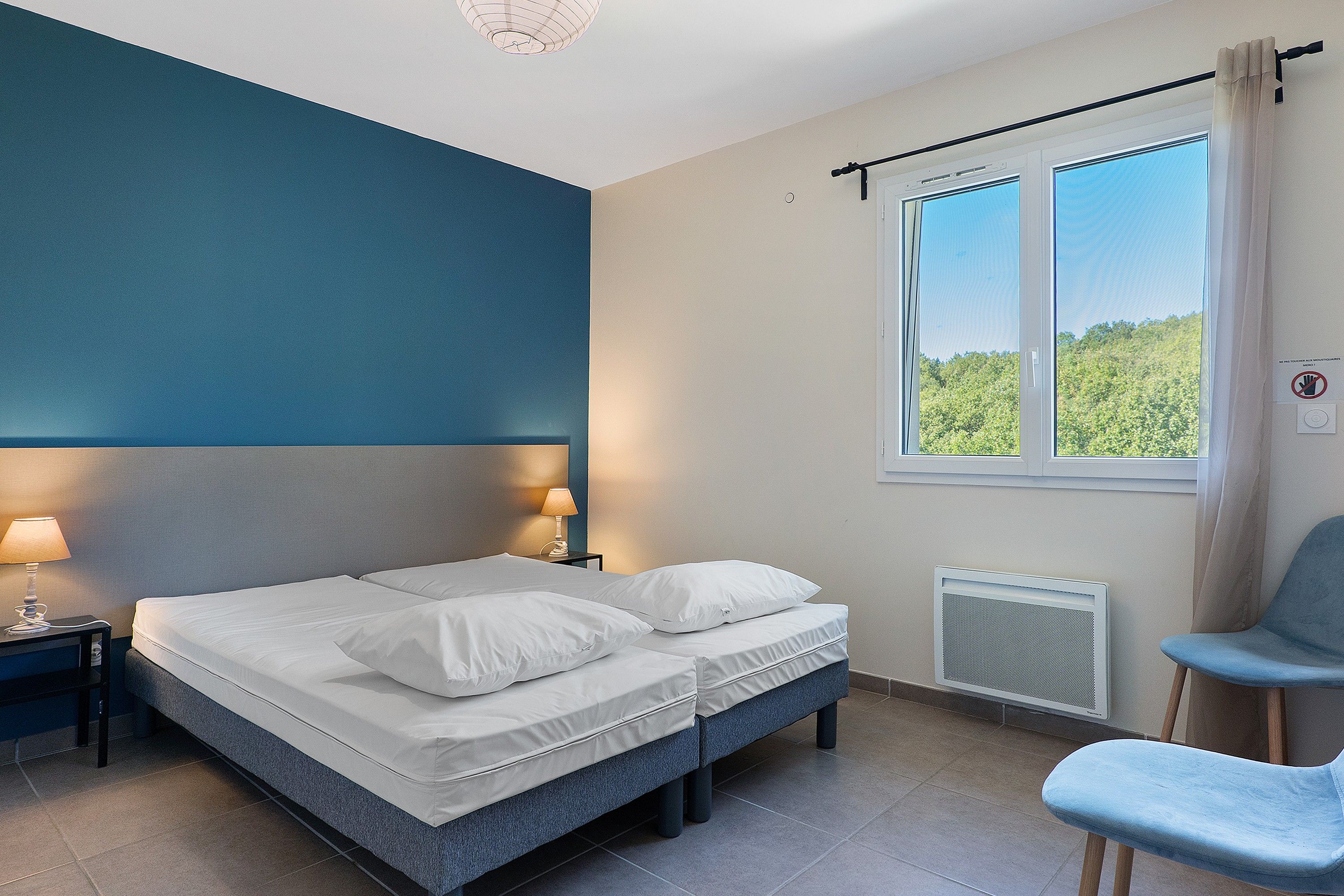 Ein Schlafzimmer mit einem Bett, einem Sessel, einem Nachttisch, einer Lampe, einem Fenster und einer Heizung.